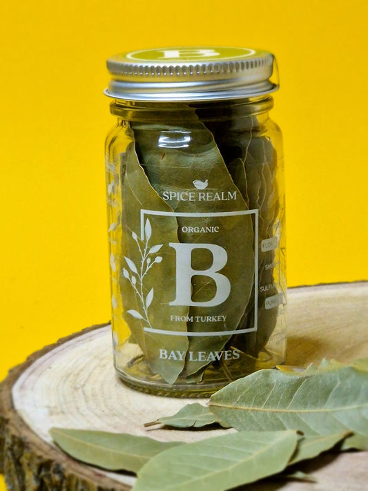 Dried bay leaves in a clear glass jar, displaying vibrant green color and rich texture, commonly used for seasoning soups, stews, and sauces.